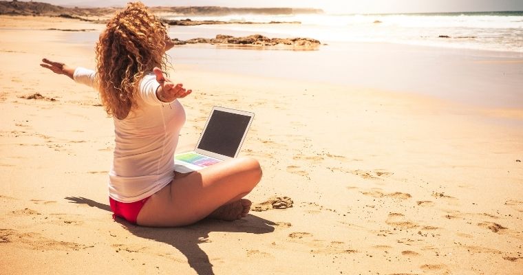 Woman sat on the beach with a laptop on her lap