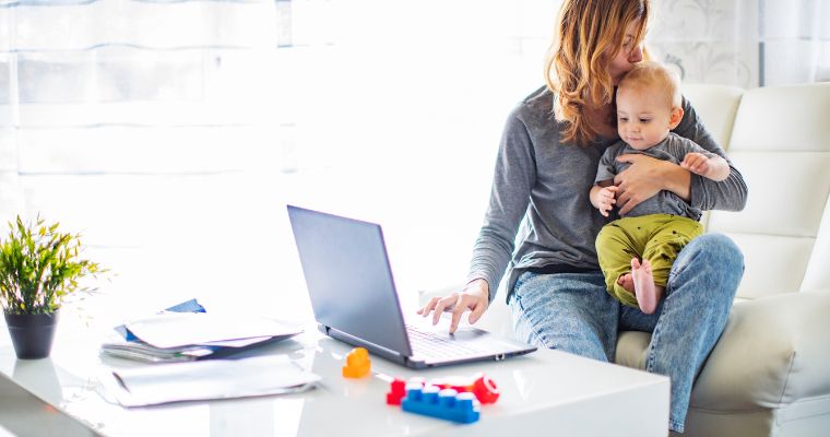 A woman working on a laptop with her baby on her lap