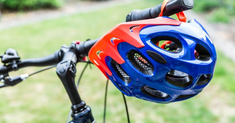 A bright blue and orange cycling helmet hanging on the handle bars of a bike